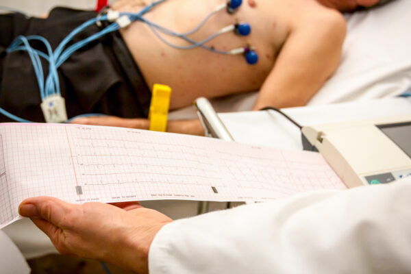 The cardiologist holding and review the electrocardiograph EKG or ECG diagram printed on grid paper.