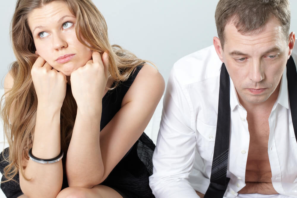 Man and woman sitting on a bed looking disappointed